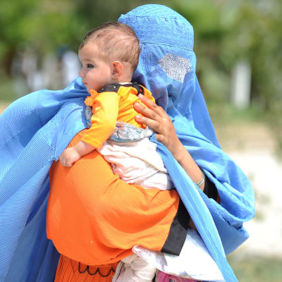En afghansk kvinna iklädd blå burka bär på ett litet barn. Hon återvänder frivilligt från Pakistan till hemlandet.