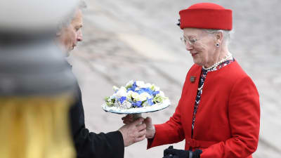 Drottning Margrethe II av Danmark iklädd röd dräkt tar emot en blombukett av president Sauli Niinistö utanför presidentens slott i Helsingfors.
