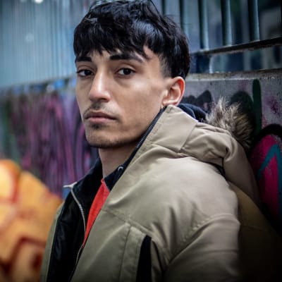 Kuvassa nuori mies seisoo graffittiseinän vieressä Vantaan Myyrmäessä.