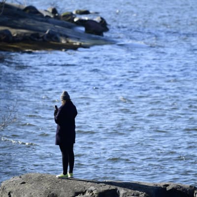 Kvinna på en strand med en mobiltelefon. Helsingfors 4.4.2020