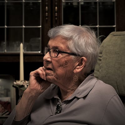 Äldre kvinna framför en bokhylla blickar ut från kameran. 