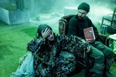 På bilden ses två personer på en rökig scen. En kvinna sitter på marken och en man i en fåtölj. Mannen håller i boken Mammuten av Jörn Donner.