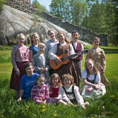Sarah Nedergård står med en gitarr i handen och barn runt omkring sig.
