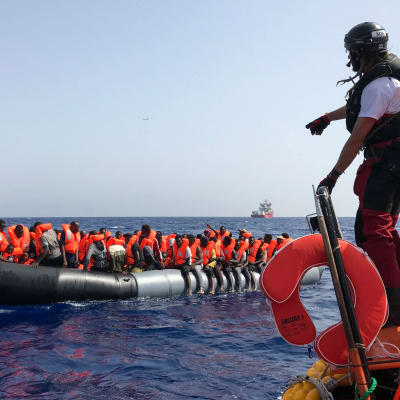 En av räddningspersonalen från fartyget Ocean Viking står på kanten av en gummibåt och förbereder sig för att rädda migranter som sitter på en annan gummibåt ute på havet.