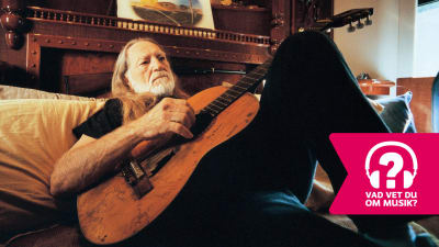 Willie Nelson spelar akustisk gitarr liggande på en säng..