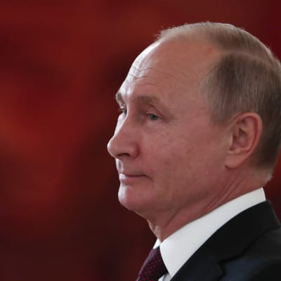 Vladimir Putin i profil mot ett rött draperi i bakgrunden.