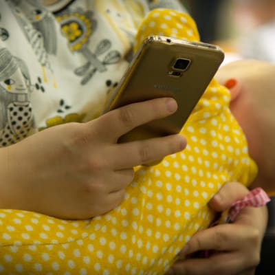 Äiti selaile kännykkänsä ja samalla rintaruokii vauvaa helsingin lapsimessuilla