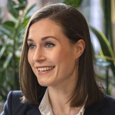 Sanna Marin ler och tittar åt sidan. Hon är iklädd kostym och har axellångt hår.