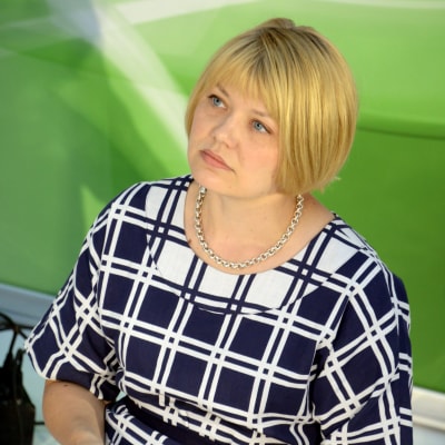 En bild på Elina Moisio - hon sitter ner och bakgrunden är grön. 