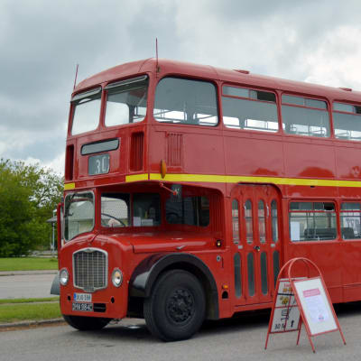 En gammal röd buss står parkerad och två personer tittar på den.