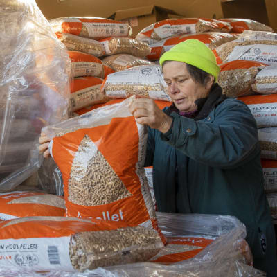 En kvinna står och håller i en säck pellet. Hon är omringad av fler säckar pelletar.