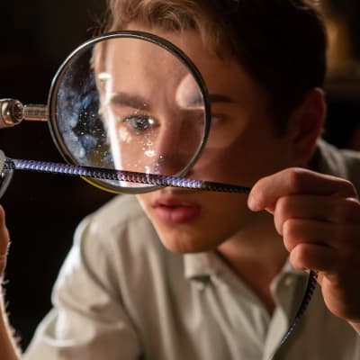 En ung man tittar på en filmremsa genom ett förstoringsglas.