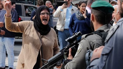 Arg palestinsk kvinna hötter med näven åt beväpnad israelisk soldat.