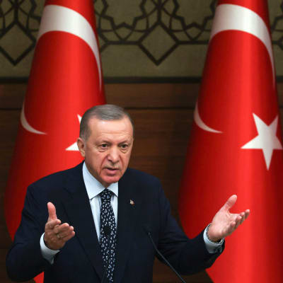 Turkiets president Recep Tayyip Erdoğan framför tre stora turkiska flaggor. 