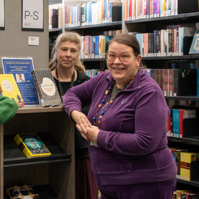Fyra kvinnor står vid några bokhyllor i ett bibliotek och tittar in i kameran.