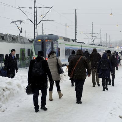 Passagerare går på en snöig perrong mot väntande tåg.