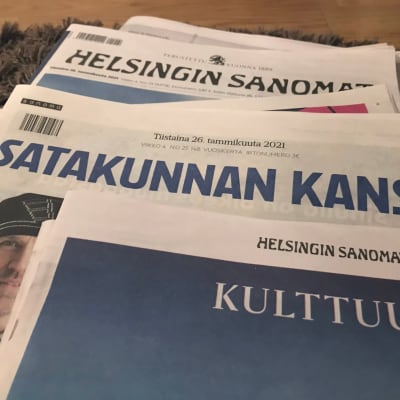 Sanomalehtiä lattialla maton päällä.