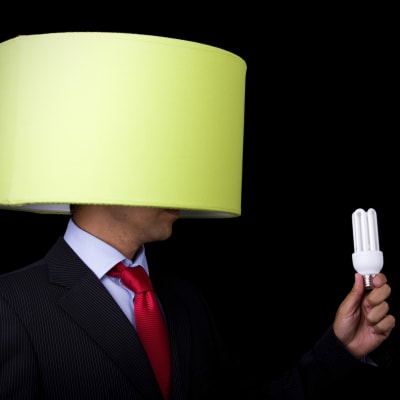 En man har en lampskärm på sitt huvud och håller i en lampa i sin hand som han håller framför skärmen.