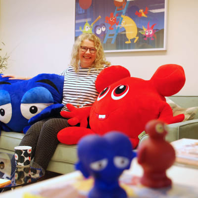 Anneli Tisell sitter i en soffa med två stora figurer från Babblarna.