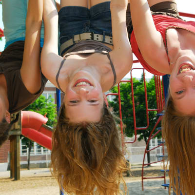 tre långhåriga flickor hänger skrattande upp och ner i en klätterställning