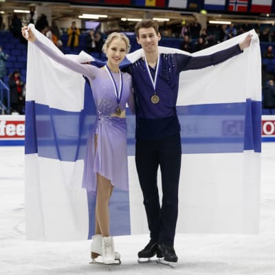 Juulia Turkkila och Matthias Versluis poserar med Finlnds flagga och bronsmedaljer.