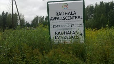 Skylt i högt gräs som berättar vilka tider Rauhala avfallscentral i Pargas har öppet.