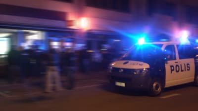 Polisbil på uppdrag på natten i Borgå. Nyfikna ungdormar på gatan.