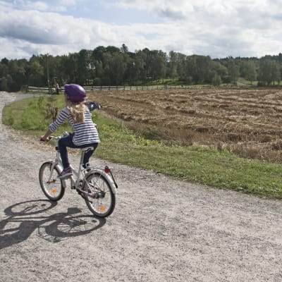 Flicka cyklar på landsväg.