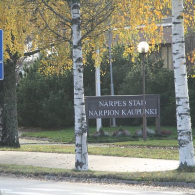 En skylt där det står Närpes stad skymtar mellan två björkar i höstskrud..