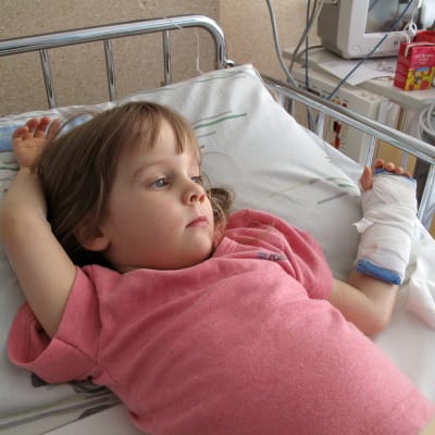 En liten flicka ligger med gipsad arm på sjukhus.