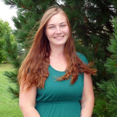 profilbild på Jennifer Molnár-Koschinsk1. Bakom en förädlad tall