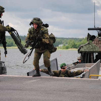 Två finska soldater kliver av en stridsbåt under en krigsövning. En chef övervakar övningen.