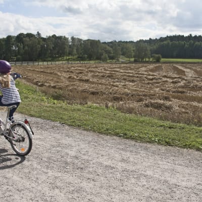Flicka cyklar på landsväg.