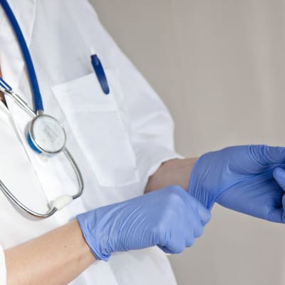 En läkare med blå plasthandskar och ett stetoskop runt halsen. 