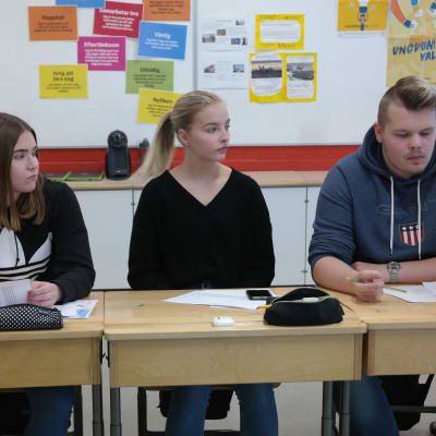 Tre elever sitter i sina pulpeter i en rad i ett klassrum, de är Cindy Henriksson, Sanni Ekblad och William Henriksson
