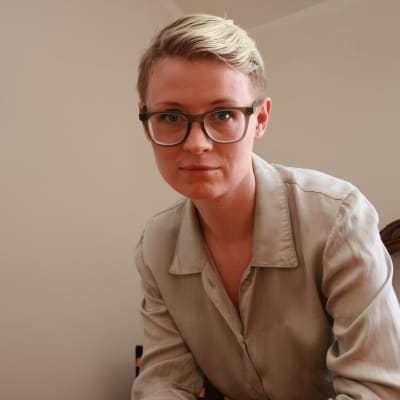 Tanja sitter på en gammal trästol och ser rakt in i kameran med ett försiktigt leende.
