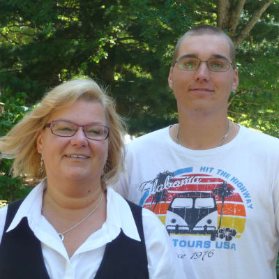 Till vänster kvinna i blont hår, till höger ung man i vit t-shirt, båda bär glasögon.