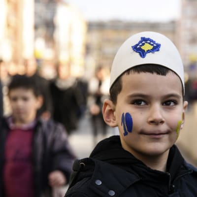 Pojke i Kosovo i traditionell albansk mössa med Kosovos flagga påsydd.