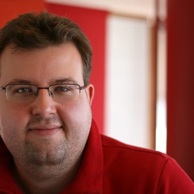 redaktören Jesper Alm på bild i en röd munkjacka.