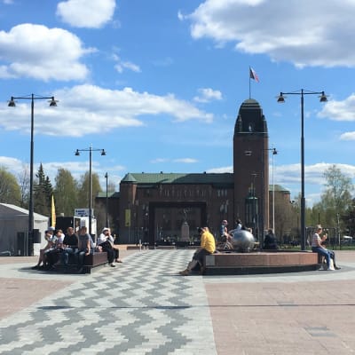 Näkymä Joensuun torilta kaupungintalolle päin kesällä vuonna 2020. Keskellä kuvaa ihmisiä istumassa suihkulähteen penkeillä.