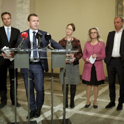 Petteri Orpo står och håller tal. I bakgrunden syns Kai Mykkänen, Sari Essayah, Päivi Räsänen och Harry Harkimo.
