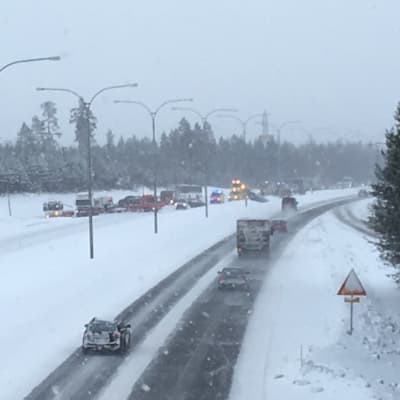 Krockade bilar, en ambulans och bärgningsfordon syns på en snöig landsvägssträcka.