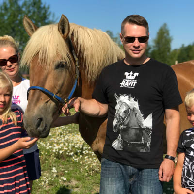 Kaksi lasta, äiti ja isä sekä perheen omistama hevonen niityllä. 