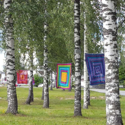 Mummon Pyykkipäivä -teokseen kuuluvia isoäidin neliöitä roikuu pyykkinaruilla koivikossa.