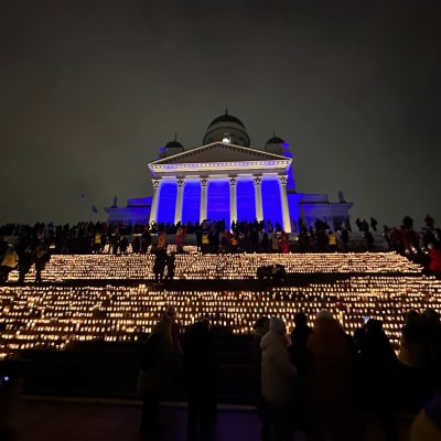 Helsingin tuomiokirkko, jossa sinistä valoa, ja kirkon edessä kynttilöitä.