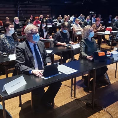 Kanta-Hämeen hyvinvointialueen aluevaltuuston edustajat istumassa pöytien äärellä isossa salissa.