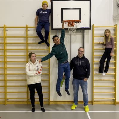Fyra barn och en vuxen står i en gymnastisal. Tre av barnen har klättrat uppför ribbor som finns vid väggen, en av dem hänger till och med i en basketkorg.