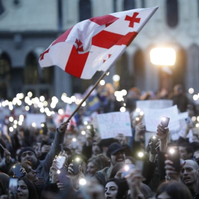 Demonstranter håller upp sina mobiltelefoner. En georgisk flagga syns i förgrunden.