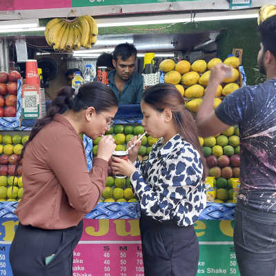 Två indiska kvinnor delar på en saft vid en fruktsaftkiosk i Delhi i Indien. De dricker samtidigt med varsitt sugrör.