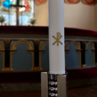 Alttarin edessä on moderni kynttilänjalka, jonka kynttilässä on kristussymboli.